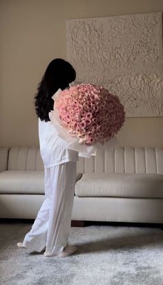 a woman holding a large bouquet of flowers in front of a white couch with a painting on the wall behind her