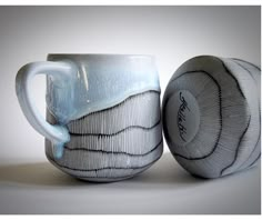 two coffee mugs sitting next to each other on a white surface with an artistic design