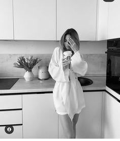 a woman in a bathrobe is holding a cup and looking at her phone