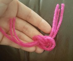 a hand holding a pink string with a knot on it