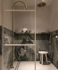 a bathroom with marbled walls and flooring, including a shower head in the corner