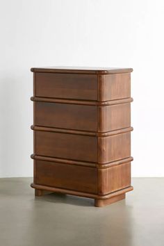 a wooden chest of drawers sitting on top of a cement floor next to a white wall