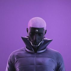 a man with a bald head wearing a purple jacket and black mask, standing in front of a purple background