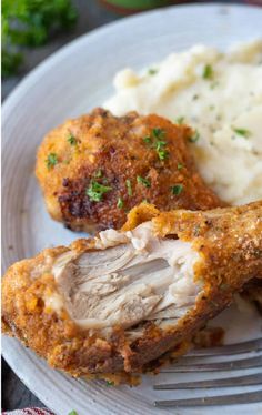 two pieces of chicken and mashed potatoes on a white plate with a silver fork