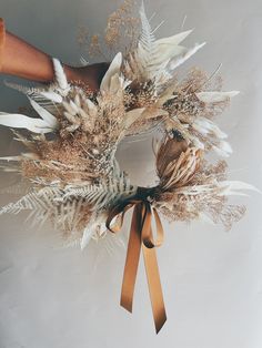 a person is holding a wreath with feathers and other things around it on a white background