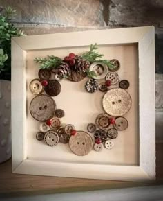 a white frame with buttons and pine cones in it on top of a table next to a potted plant