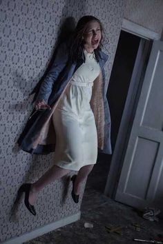 a woman in a white dress and coat leaning against a wall