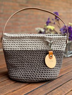 a gray and white basket with a wooden tag on it sitting on a table next to purple flowers