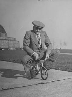 an old man in a suit and tie riding a bike