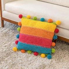 a multicolored pillow with pom - poms sits on the floor next to a white couch