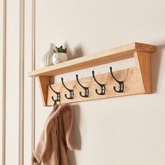 a coat rack with five hooks and two coats hanging on the wall next to a potted plant