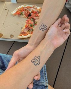 two people with matching tattoos on their arms holding hands near pizza boxes and one has a slice of pizza