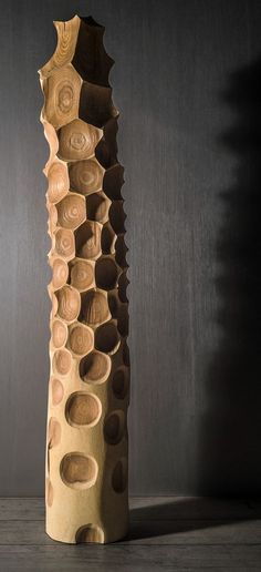 a tall wooden sculpture with holes in it's center on a wood floor next to a wall