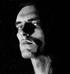 black and white photograph of a man with long hair looking off to the side in darkness