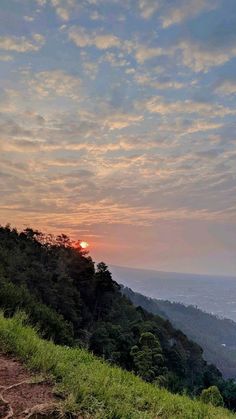 the sun is setting on top of a hill with trees and grass in front of it