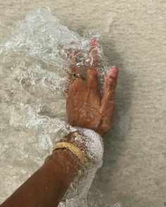 a person's hand in the water with their feet covered by sand and plastic