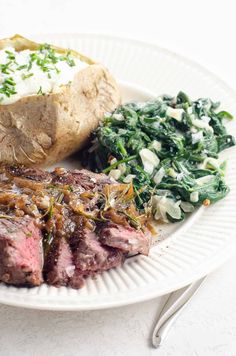 a white plate topped with steak, potatoes and spinach next to a baked potato