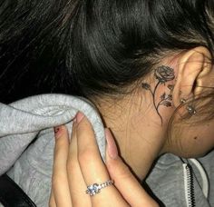 a woman with a flower tattoo on her left side behind her ear, looking down at the ground