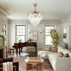 a living room filled with furniture and a chandelier above a fire place in front of a piano