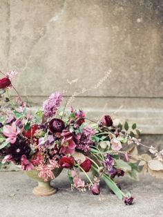 a vase filled with lots of flowers sitting on top of a cement floor next to a wall