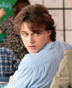 a young man sitting at a table with his hand on his shoulder and looking off to the side