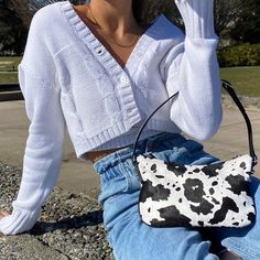 a woman sitting on the ground holding a cell phone to her ear and wearing a cow print purse