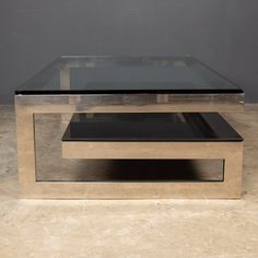 a glass and metal coffee table sitting on top of a marble slabd floor in front of a gray wall