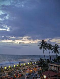 cars are parked on the side of the road next to the ocean at dusk with palm trees in the foreground