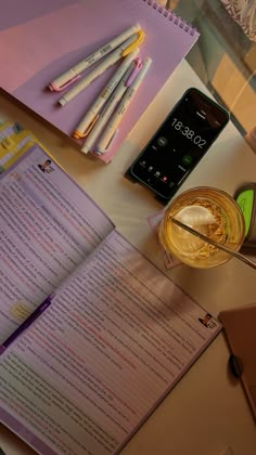 an open book sitting on top of a table next to a cup of liquid and pencils