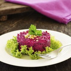 a white plate topped with beet and lettuce covered in sauce next to a fork