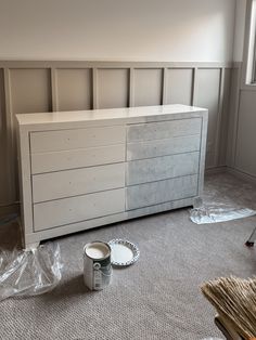 a white dresser sitting on top of a carpeted floor next to a can of paint