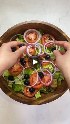 two hands reaching for onions and tomatoes on a salad in a wooden bowl with lettuce