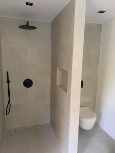 a white bathroom with a black shower head in the corner and an open toilet on the other side