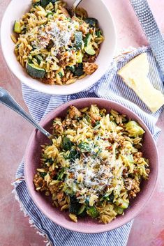 two bowls filled with pasta and vegetables on top of a pink table cloth next to silverware