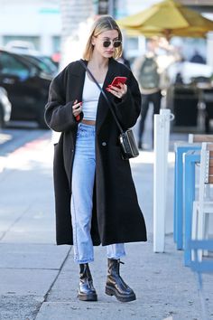 a woman in black coat and jeans looking at her cell phone while walking down the street