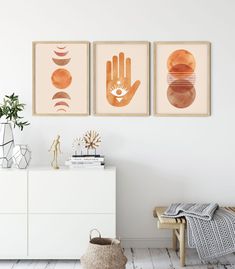 three framed art prints on the wall above a white dresser with a plant and vase