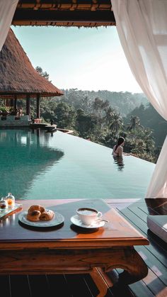 a table with food on it in front of a pool and some people sitting at the edge