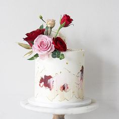 there is a white cake with red and pink flowers on the top it sits on a stand