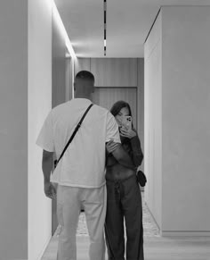 a man and woman standing next to each other in a hallway with white walls on either side