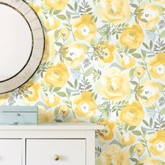 a white dresser sitting next to a mirror on top of a wooden cabinet in front of a yellow flowered wallpaper