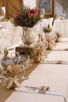 the table is set with wine glasses, silverware and flowers in a vase on top of burlap