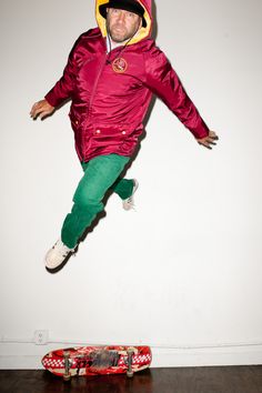 a man is jumping in the air with his skateboard behind him and wearing a red jacket