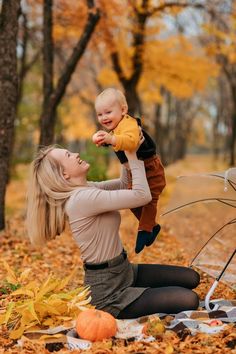 a woman holding a baby in her arms while sitting on the ground surrounded by leaves