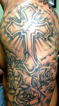 a cross and roses tattoo on the back of a man's shoulder, which is covered in black ink