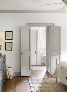 a bedroom with white walls and wooden floors, two doors open to reveal another room