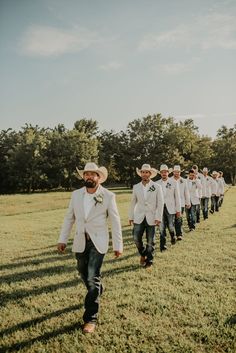 a group of men in white suits and hats walking across a grass covered field next to each other