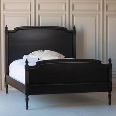 a black bed frame with white sheets and pillows on it, in front of a paneled wall