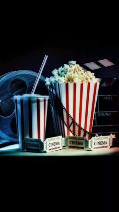 two cups filled with popcorn sitting on top of a table next to film reels