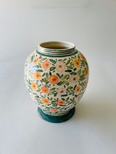 a vase with flowers painted on it sitting on a white tableclothed surface in front of a plain background