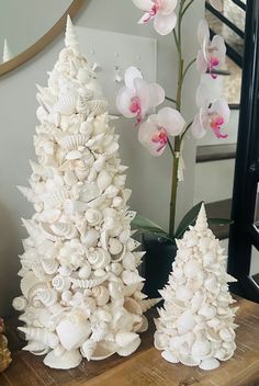 three white christmas trees on a table with pink orchids in the foreground and a mirror behind them